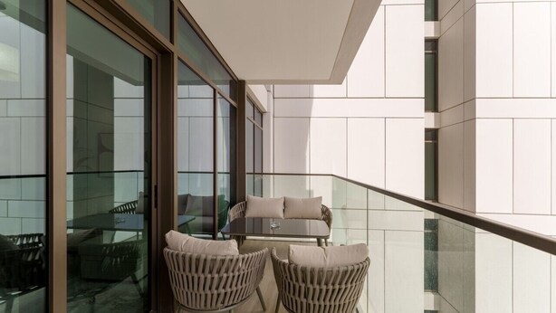 Ein Balkon mit Glastrennwand, einer Couch und zwei Stühlen.