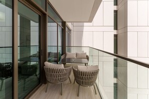 Een balkon met glazen hekwerk, een bank en twee stoelen.
