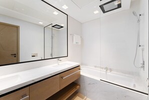 A modern bathroom with a large mirror, a white sink, a wooden vanity, and a glass-enclosed shower area.