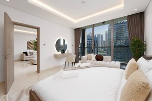 A modern hotel room with a large bed, a seating area, a round mirror, and a view of the cityscape.