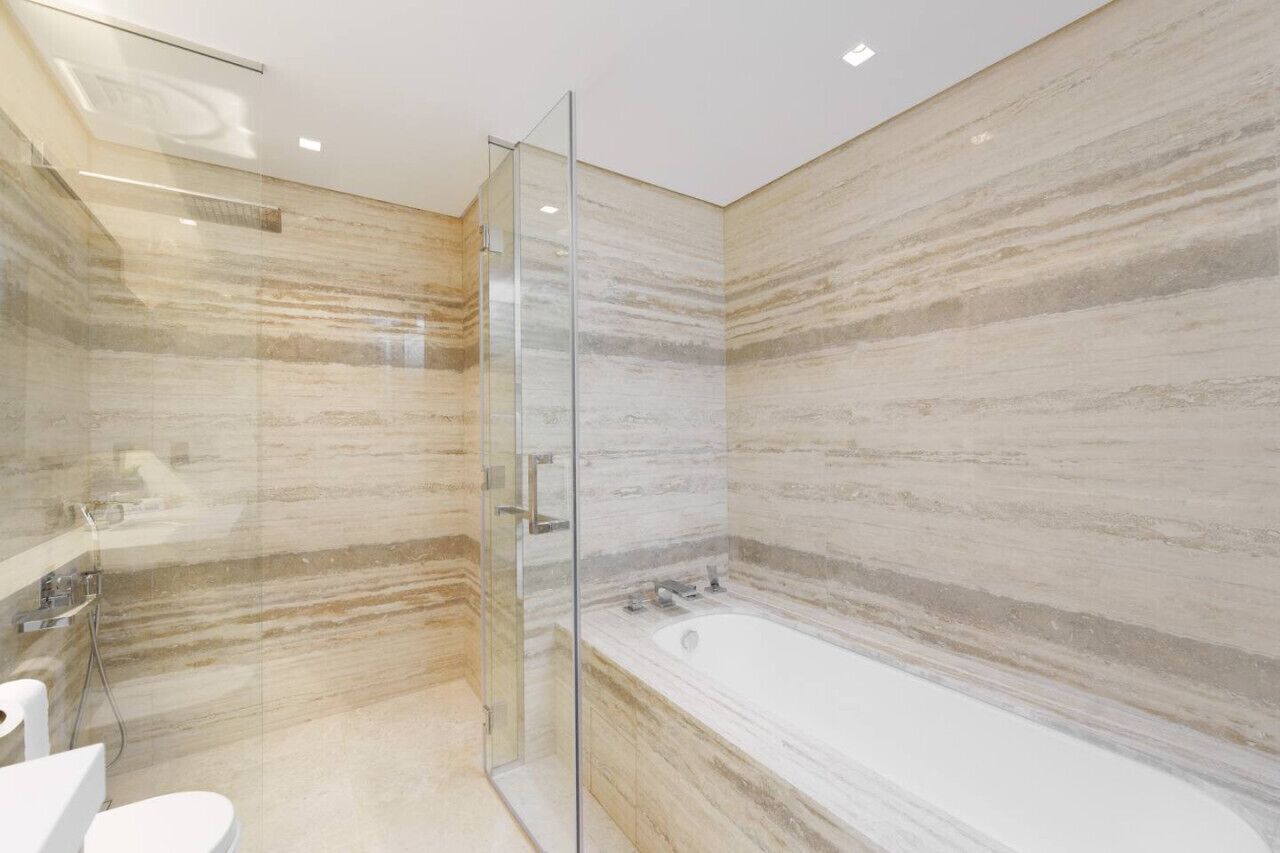 Un baño moderno con cabina de ducha de vidrio, bañera y paredes de mármol.