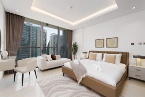 Quarto de hotel moderno com uma cama grande, uma escrivaninha, um sofá e vista para a paisagem urbana.