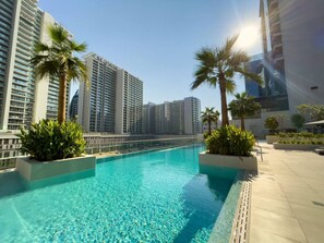 A swimming pool with clear blue water, surrounded by palm trees and modern buildings in the background.