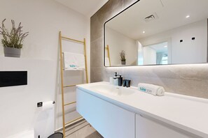 A modern bathroom with a white sink, a large mirror, and a towel rack.