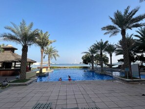 En swimmingpool med palmer, en bygning med stråtækt tag og havudsigt.
