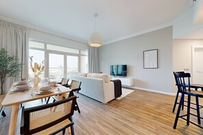 A modern living room with a sofa, dining table set for four, and a TV mounted on the wall.