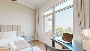 Ein Hotelzimmer mit einem Bett, einem Schreibtisch mit einem Laptop, einem Stuhl, einer Lampe und einem großen Fenster mit Vorhängen.
