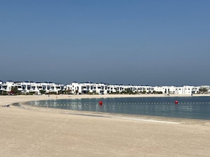 Un hotel frente a la playa con edificios blancos, una playa arenosa y un mar tranquilo.