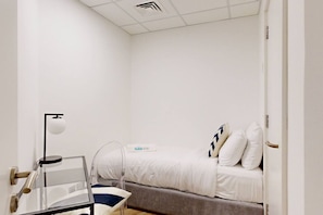 Una habitación pequeña y blanca con una cama individual, una mesita de noche, una lámpara y un letrero que dice "Suiteable".