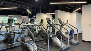 A gym with multiple treadmills and elliptical machines, arranged in rows with mirrors on the walls.