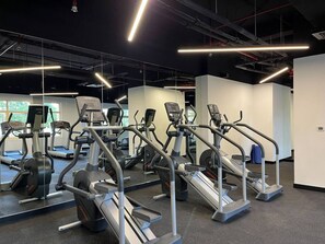 Une salle de sport équipée de nombreux tapis de course et d’appareils elliptiques, disposés en rangées avec des miroirs sur les murs.