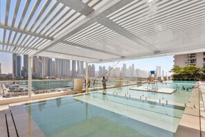 A rooftop infinity pool with a city skyline view, a covered area with a white roof, and a lifeguard stand.