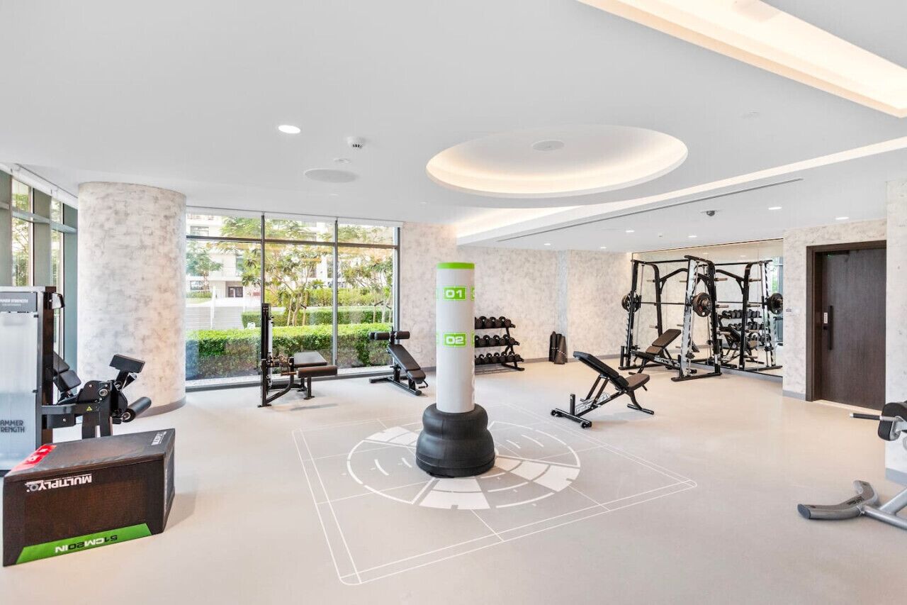 Een moderne sportschool met diverse fitnessapparaten, een grote pilaar met genummerde secties en grote ramen met uitzicht op groen.