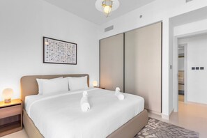 A modern hotel room with a large bed, a bedside table with a lamp, a framed artwork on the wall, and a sliding door closet.