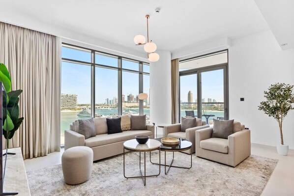 A modern living room with a sofa, two armchairs, a coffee table, and a view of a cityscape through large windows.
