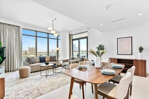 A modern living room with a dining area, large windows, and a city view.