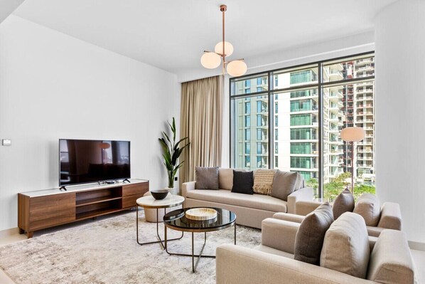 A modern living room with a flat-screen TV, a sofa, a coffee table, and a large window with a city view.