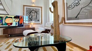 A modern living room with a glass coffee table, a mounted TV displaying animated characters, and two framed artworks. - LE PETIT LOFT du 10Honfleur (Honfleur)