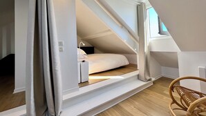 A bedroom with a sloped ceiling, a bed, a bedside table, a chair, and a window. - LE PETIT LOFT du 10Honfleur (Honfleur)