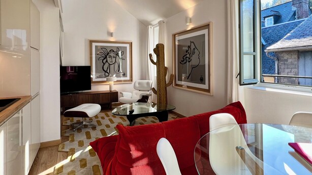 A modern living room with a glass dining table, red and white chairs, a white sofa, and a large window with a view of a blue house. - LE PETIT LOFT du 10Honfleur (Honfleur)
