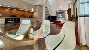 A modern kitchen with a glass dining table and chairs, a wooden floor, and a staircase leading to an upper level. - LE PETIT LOFT du 10Honfleur (Honfleur)