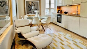 A modern kitchen with white cabinetry, a dining area with white chairs, and a large window providing natural light. - LE PETIT LOFT du 10Honfleur (Honfleur)