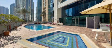 A rooftop swimming pool with a geometric tile design, surrounded by lounge chairs and potted plants.
