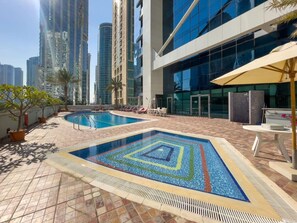 A rooftop swimming pool with a geometric tile design, surrounded by lounge chairs and potted plants.