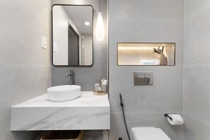 A modern bathroom with a marble sink, a mirror, a towel dispenser, and a toilet.