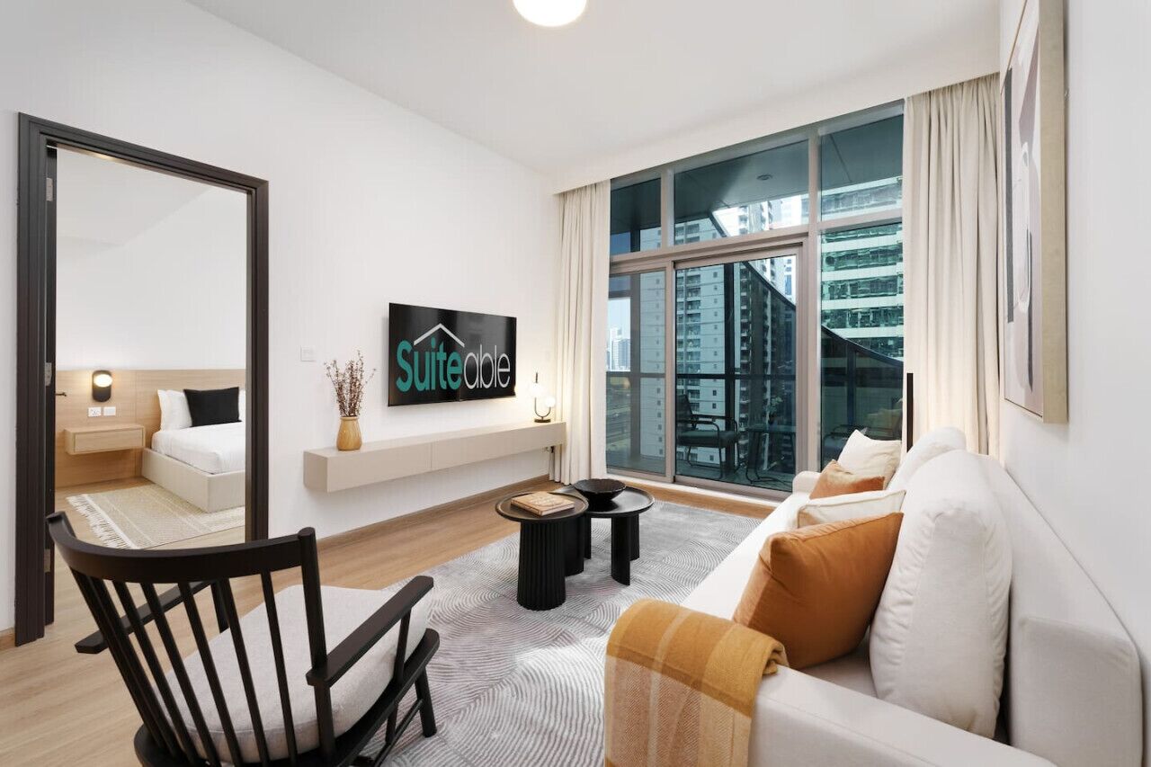 A modern living room with a sofa, a chair, a TV, and a large window with a city view.