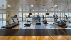 Une salle de sport équipée de tapis de course, de vélos elliptiques et de vélos d’exercice, dotée de grandes fenêtres et d’un plancher en bois.