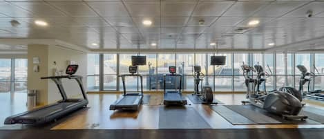 Une salle de sport équipée de tapis de course, de vélos elliptiques et de vélos d’exercice, dotée de grandes fenêtres et d’un plancher en bois.