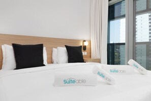 Une chambre d’hôtel avec un lit bien fait, deux oreillers, une table de chevet avec une lampe et une fenêtre donnant sur la ville.