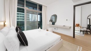 Une chambre d’hôtel moderne, dotée d’un grand lit, d’un miroir, d’une petite table et offrant une vue sur la ville grâce à de grandes fenêtres.
