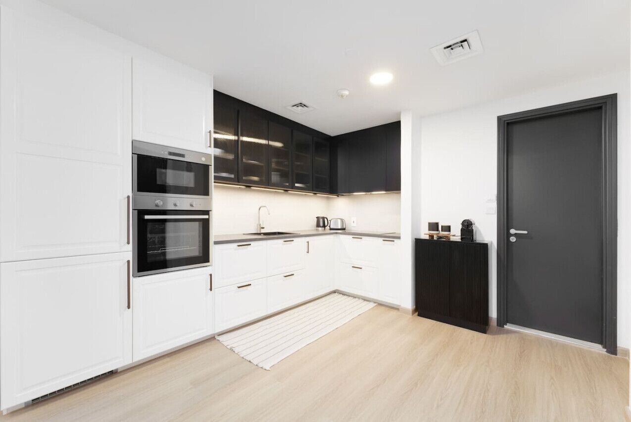 A modern kitchen with white cabinetry, a built-in oven, and a black countertop.