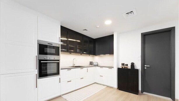 Une cuisine moderne avec des meubles blancs, un four encastré et un plan de travail noir.