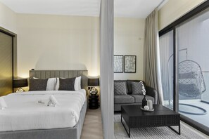 A modern hotel room with a large bed, a sofa, a coffee table, and a balcony with a hanging chair.