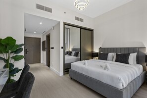 A modern hotel room with a large bed, a desk with a chair, and a potted plant. - Studio Retreat with Canal and Burj Khalifa Views (Dubai)