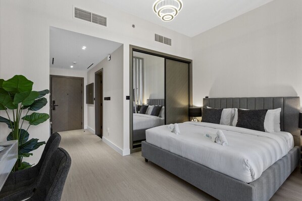 A modern hotel room with a large bed, a desk with a chair, and a potted plant.
