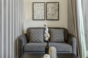 A grey sofa with patterned cushions, a vase with white flowers, and two framed abstract artworks on the wall.