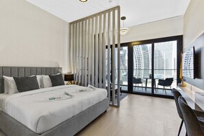 A modern hotel room with a large bed, a desk, and a balcony with a city view.