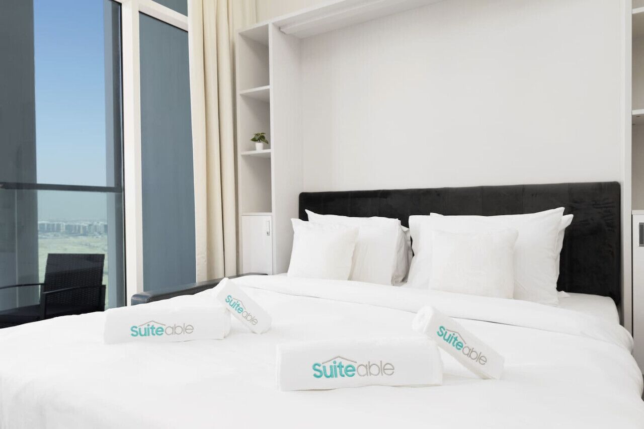 Una habitación de hotel con cama, ropa de cama blanca, cabecera negra y ventana con vistas.