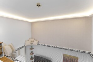 A corner room with a mesh partition, a ceiling-mounted smoke detector, and a small table with a basket and a cushion.