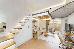 Un interior moderno con una escalera de madera, una sala de estar con sofá y mesa de centro, y un comedor con mesa y sillas.