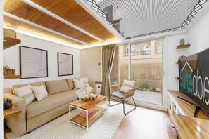 A modern living room with a wooden ceiling, a sofa, a coffee table, a chair, and a large window with a view of the outside. - Extraordinary Loft Living in JVC by Suiteable (Dubai)