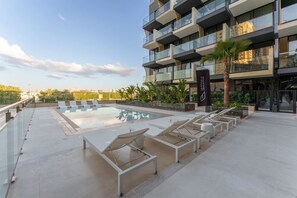 A modern building with a rooftop pool area, including lounge chairs and a palm tree. - Premium Living Apartment in JVC by Suiteable (Dubai)