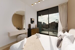 A modern bedroom with a large bed, a round mirror, a dresser, and a view of the city through a large window.
