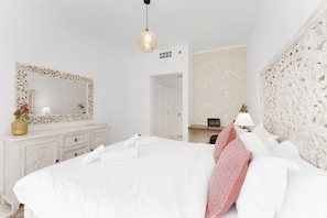 A bedroom with a large bed, a dresser, a mirror, and a desk with a lamp.