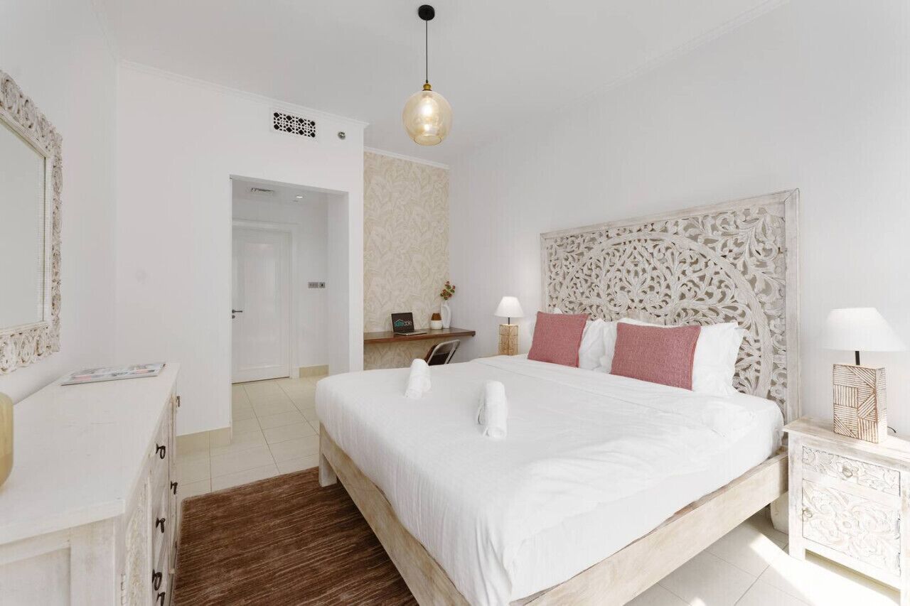 A spacious bedroom with a large bed, a bedside table with a lamp, a decorative headboard, and a wardrobe.