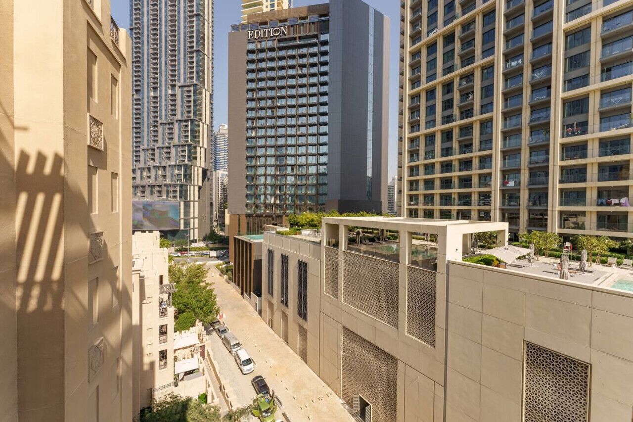A modern high-rise building with a prominent "EDITION" sign, surrounded by other tall buildings and a street with parked cars.